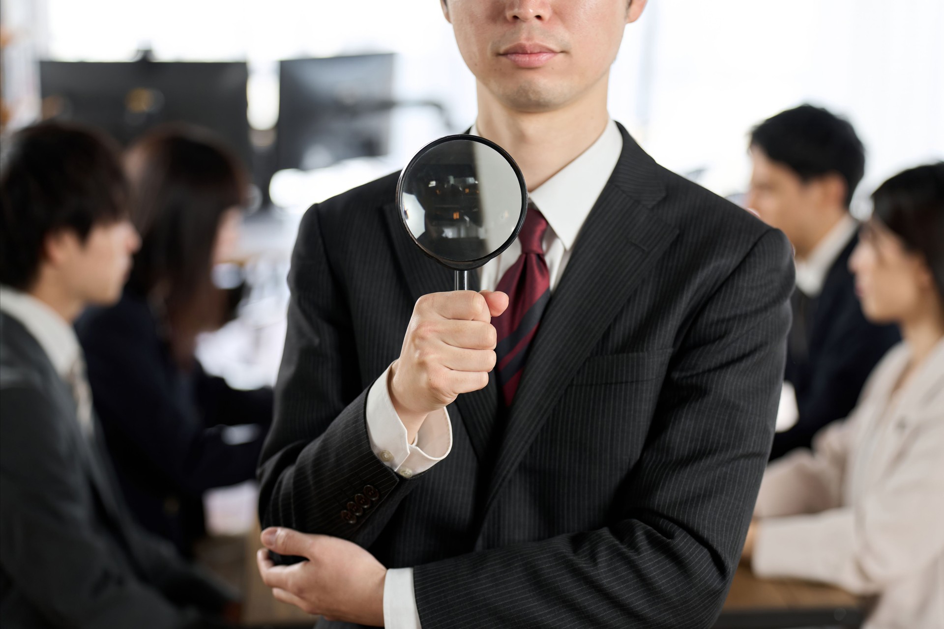 Asian businessman holding a magnifying glass and uncovering fraud